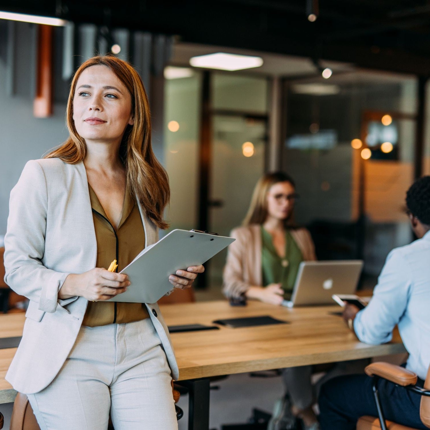 Frau lehnt mit einem Klemmbrett an einem Schreibtisch