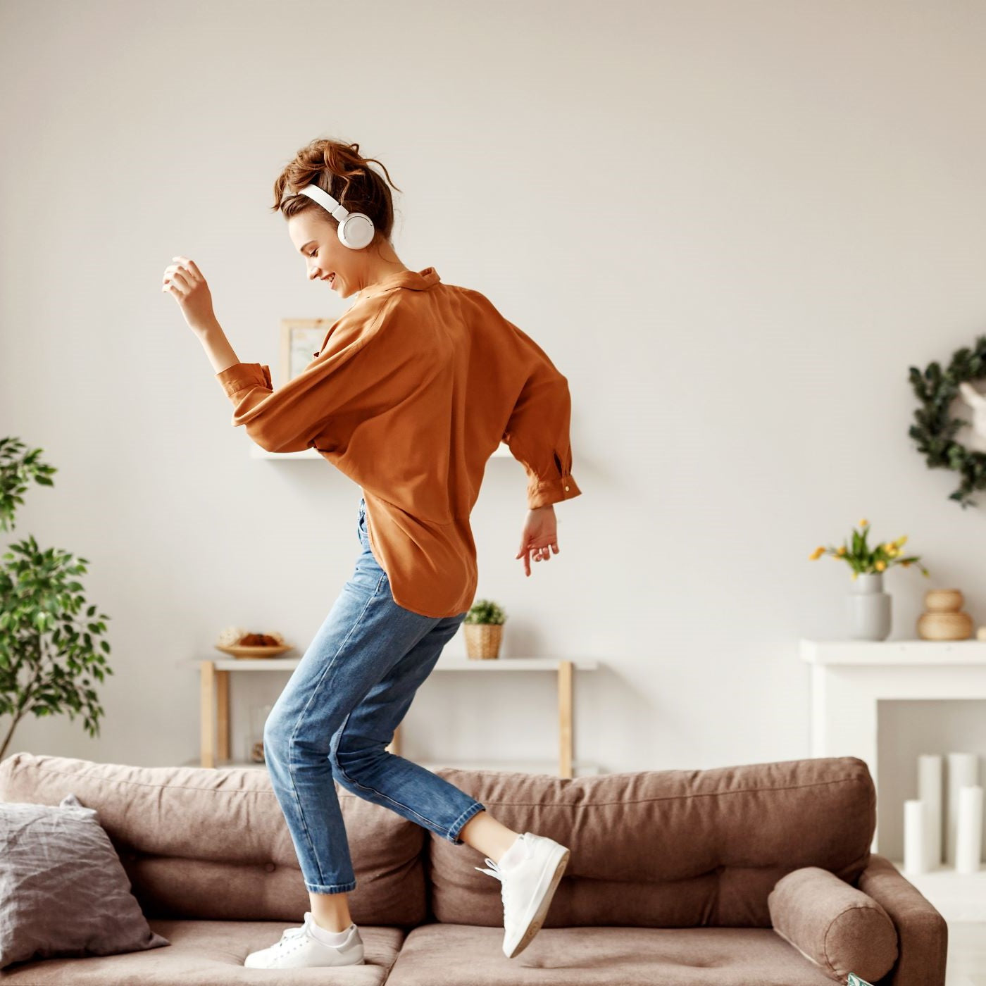 Frau tanzt mit Kopfhörern auf dem Sofa