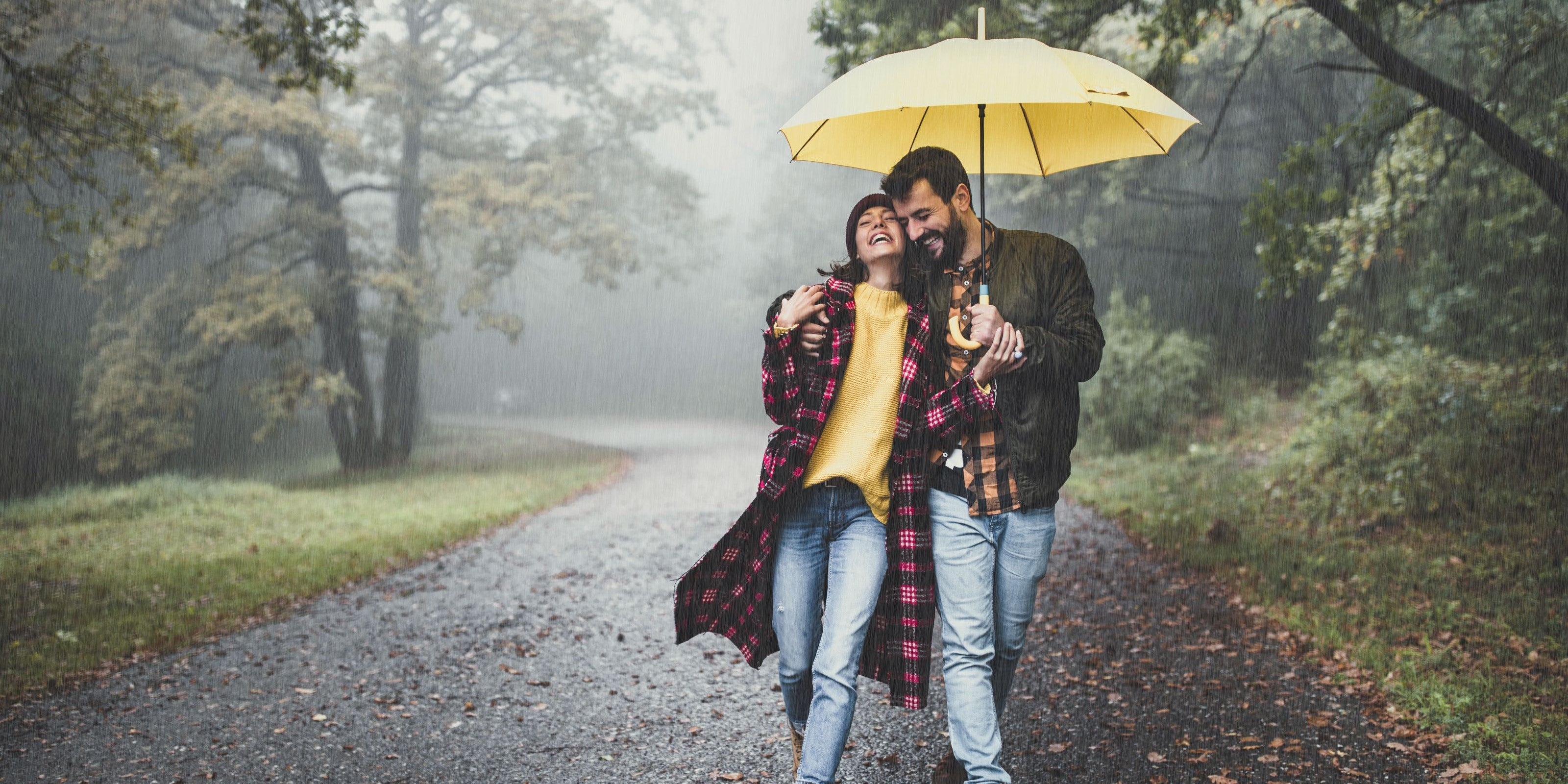 Paar geht im Regen mit einem gelben Regenschirm spazieren