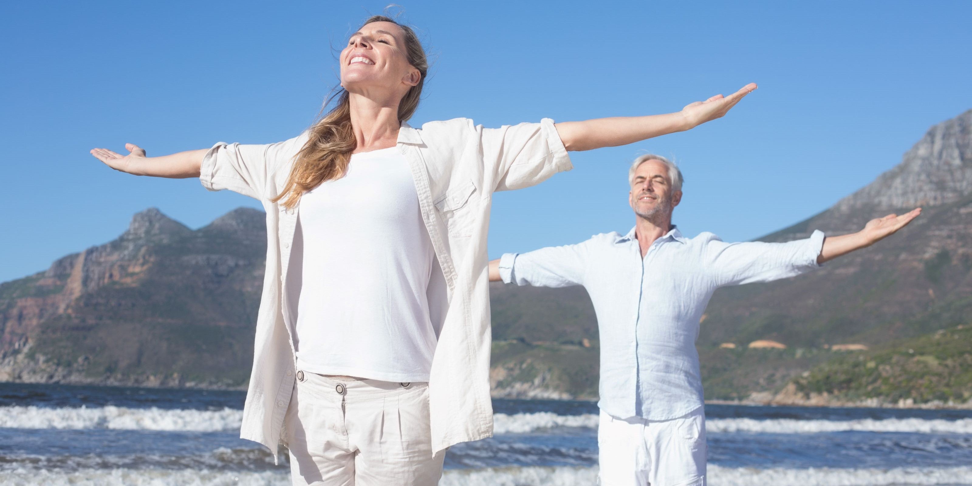 Älteres Paar meditiert am Strand mit ausgestreckten Armen