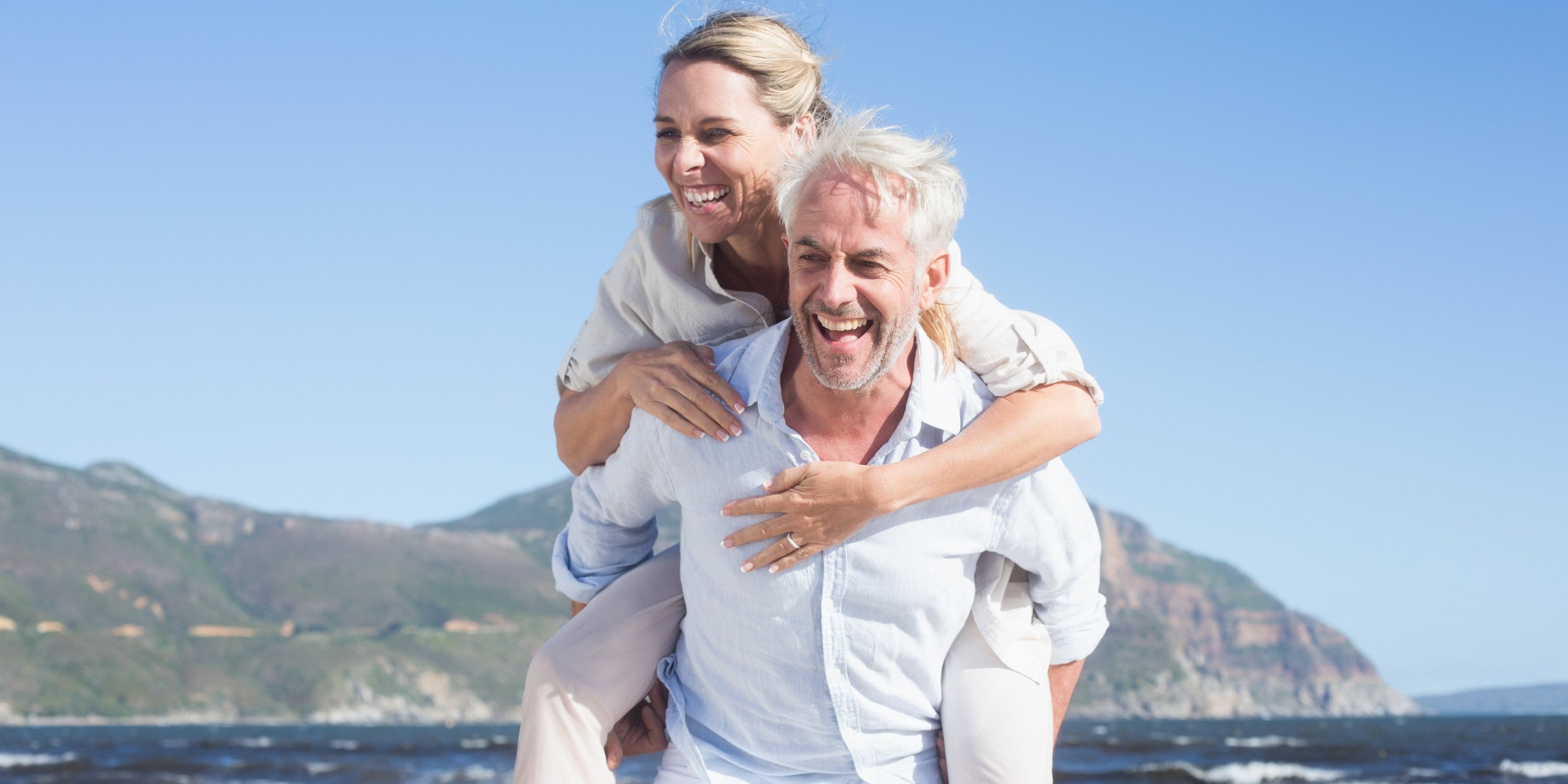 Mann trägt Frau Huckepack am Strand