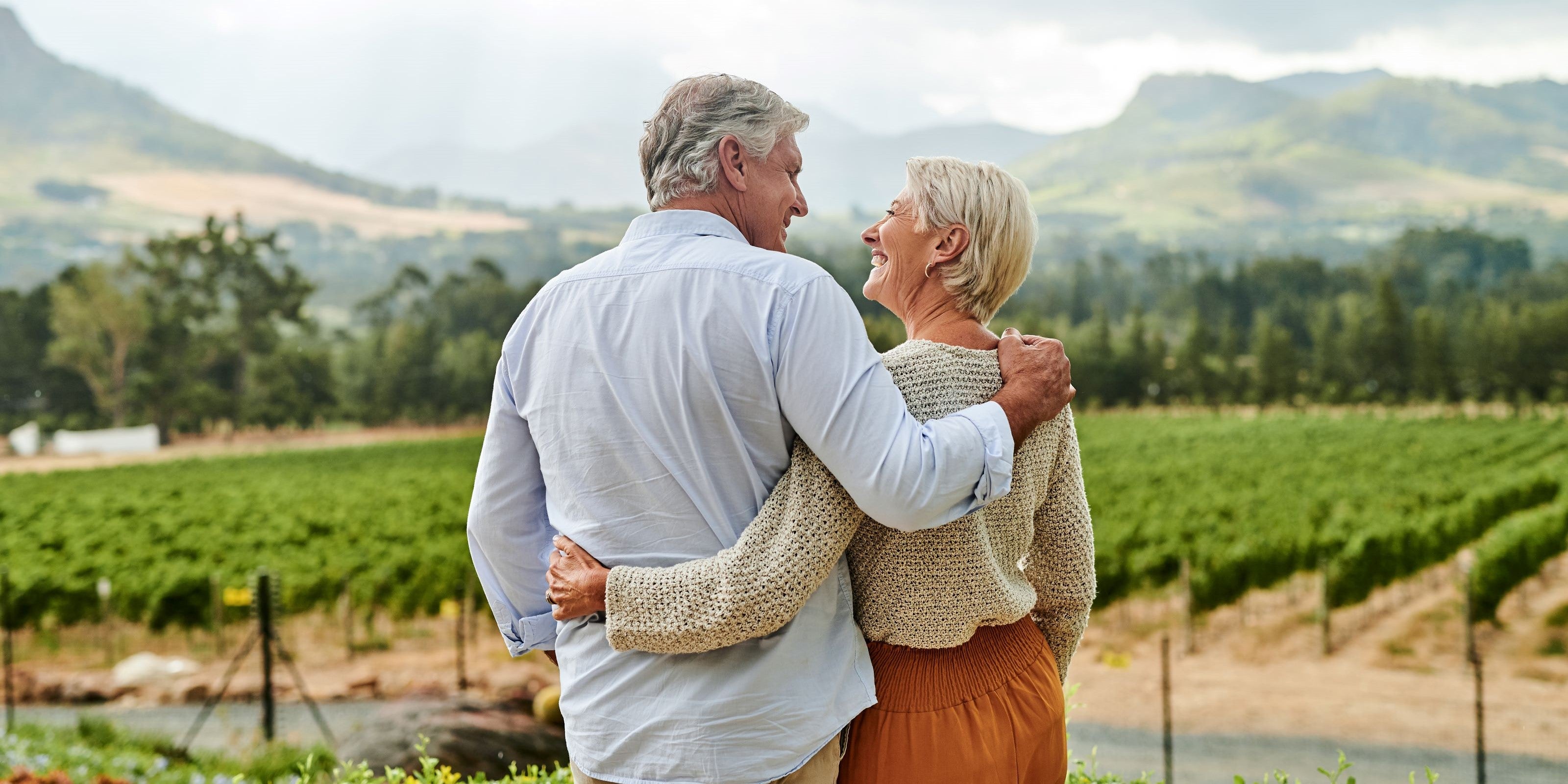 Älteres Paar steht Arm in Arm vor einem Weinberg