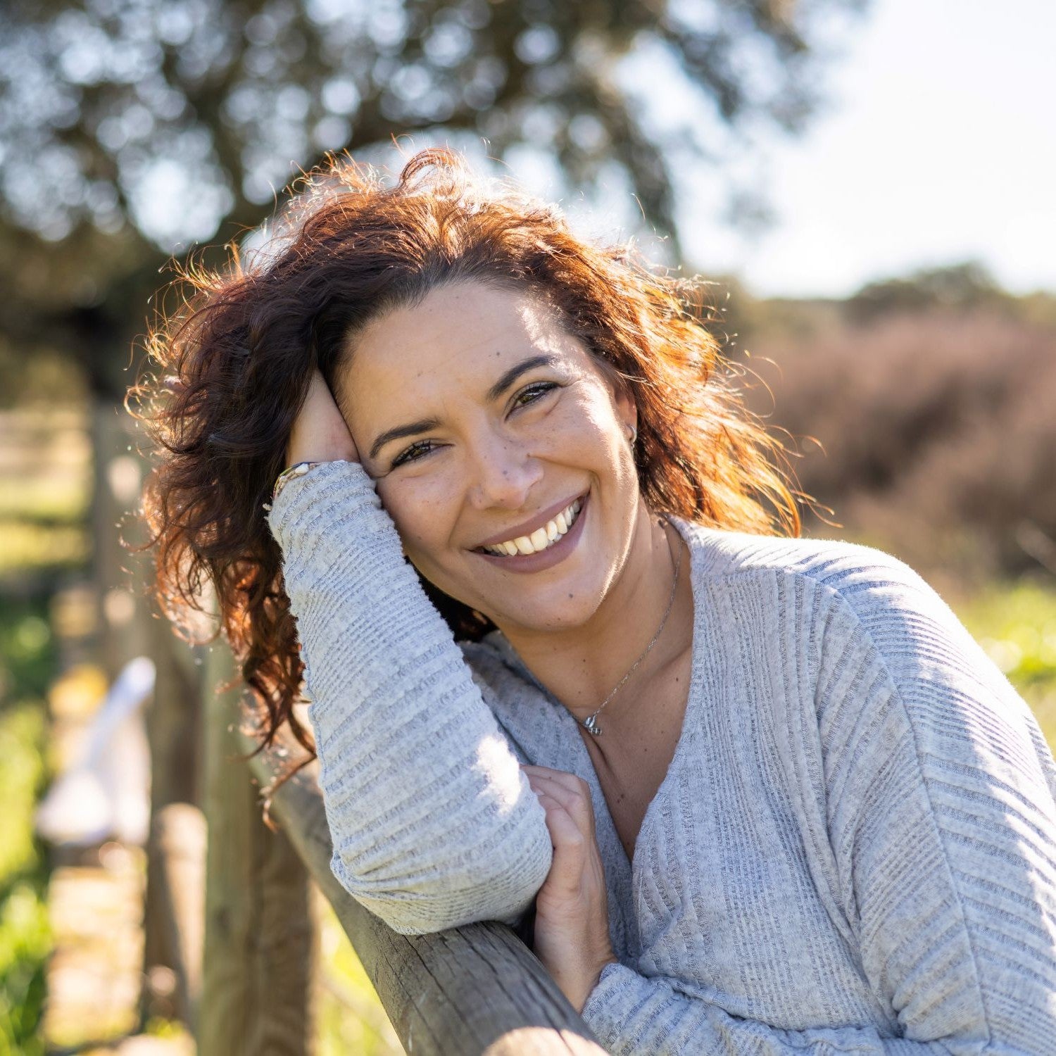 Frau lehnt sich an einen Holzzaun und lächelt in die Kamera