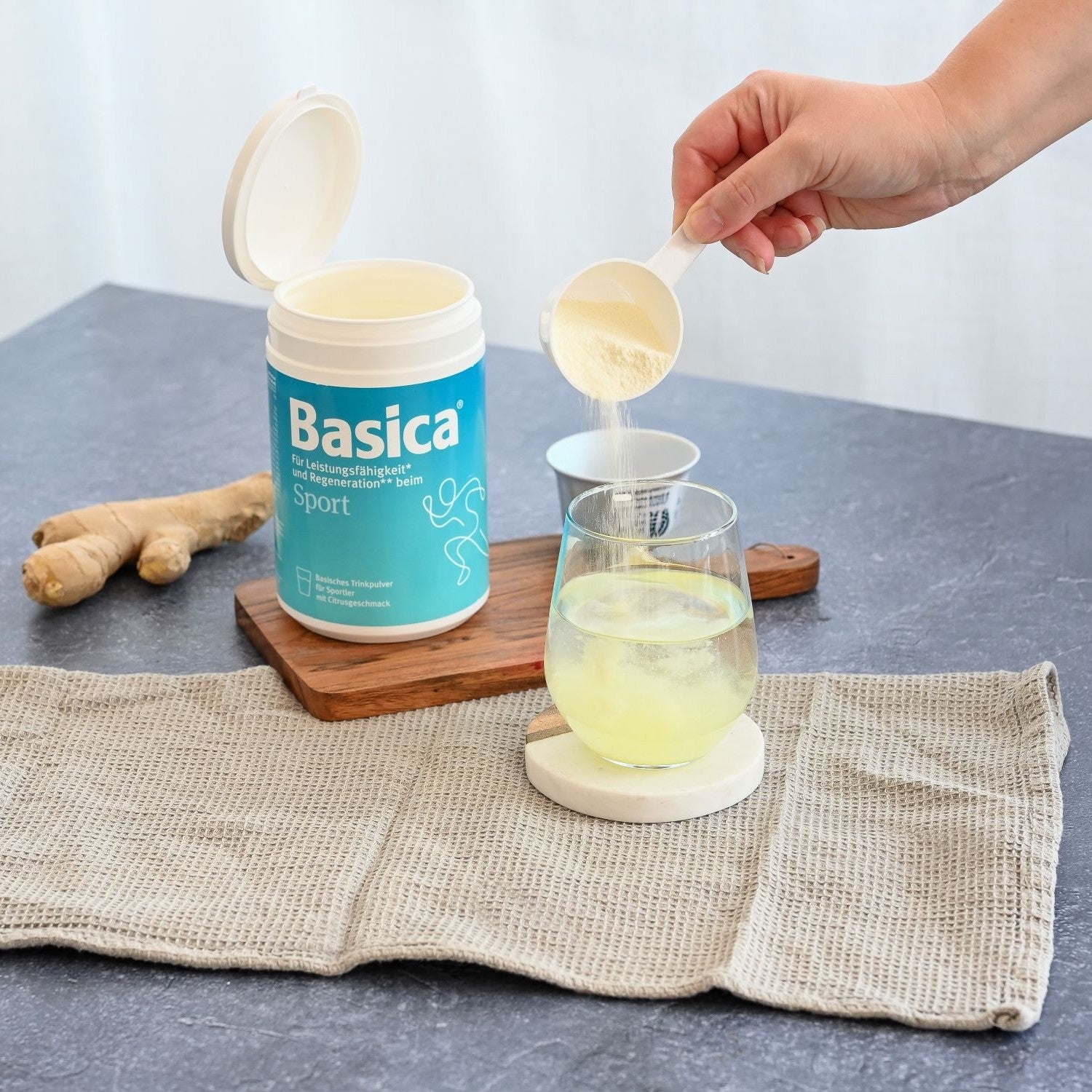 Frau schüttet Basica Sport in ein Glas mit Wasser