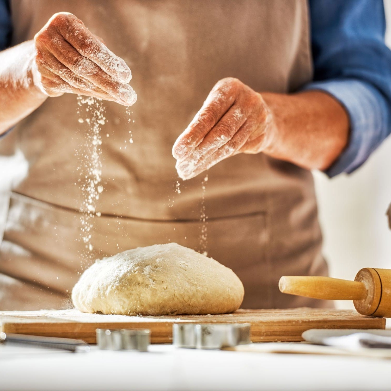 Person streut Mehl über einen Teig