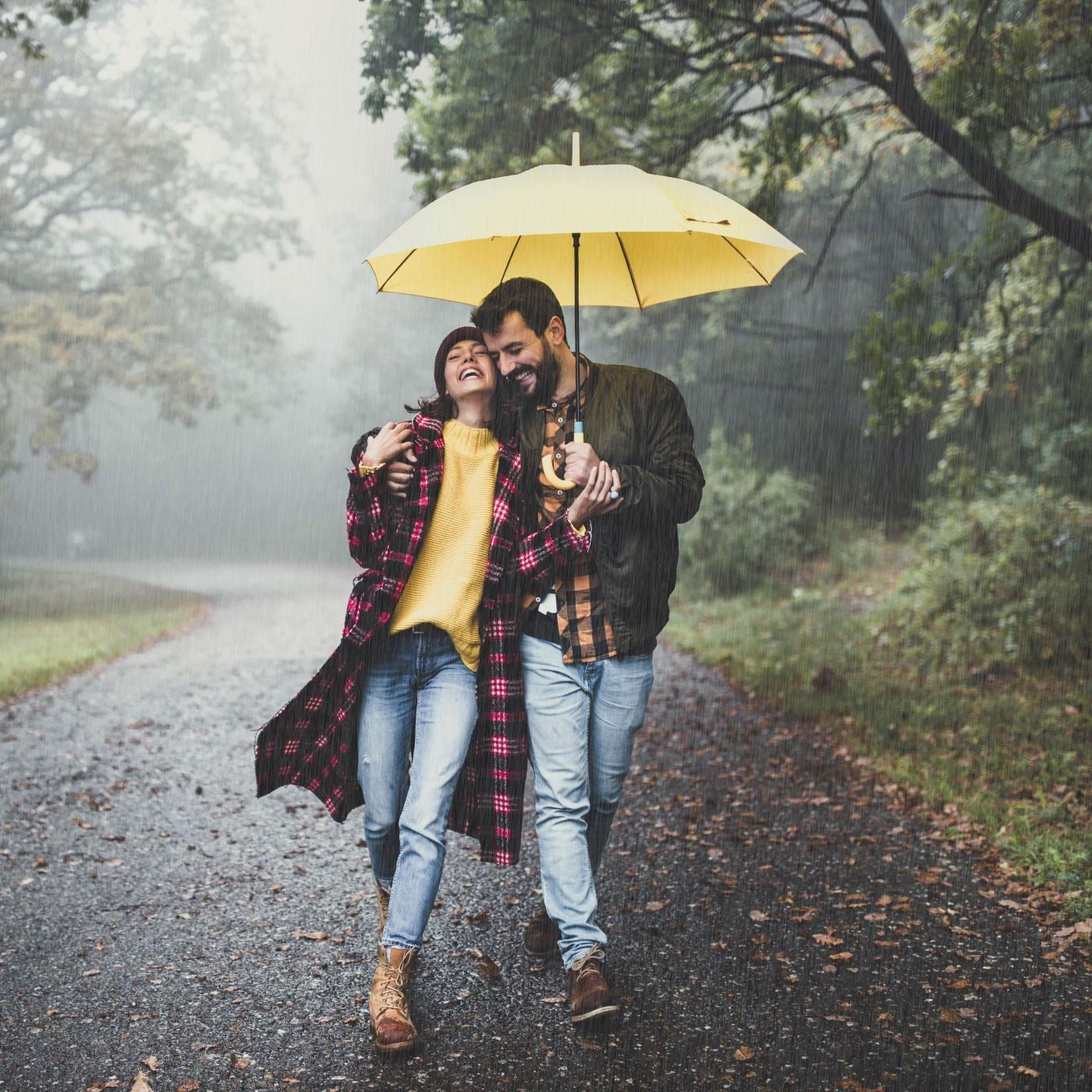 Paar geht im Regen mit einem gelben Regenschirm spazieren