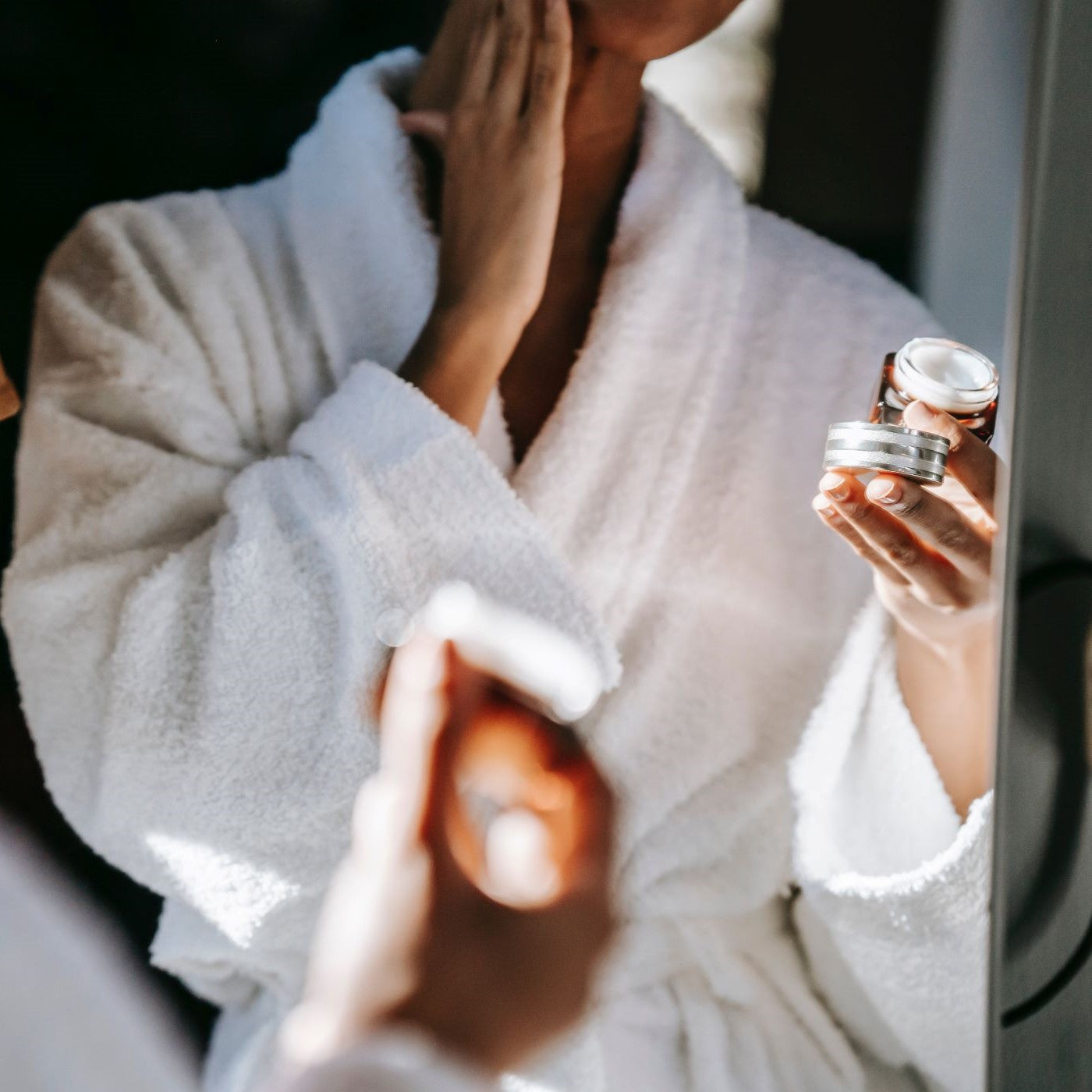 Frau hält einen Cremetiegel und cremt sich das Gesicht ein