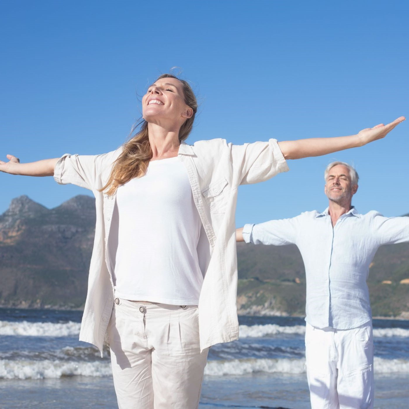Älteres Paar meditiert zusammen am Strand mit ausgestreckten Armen
