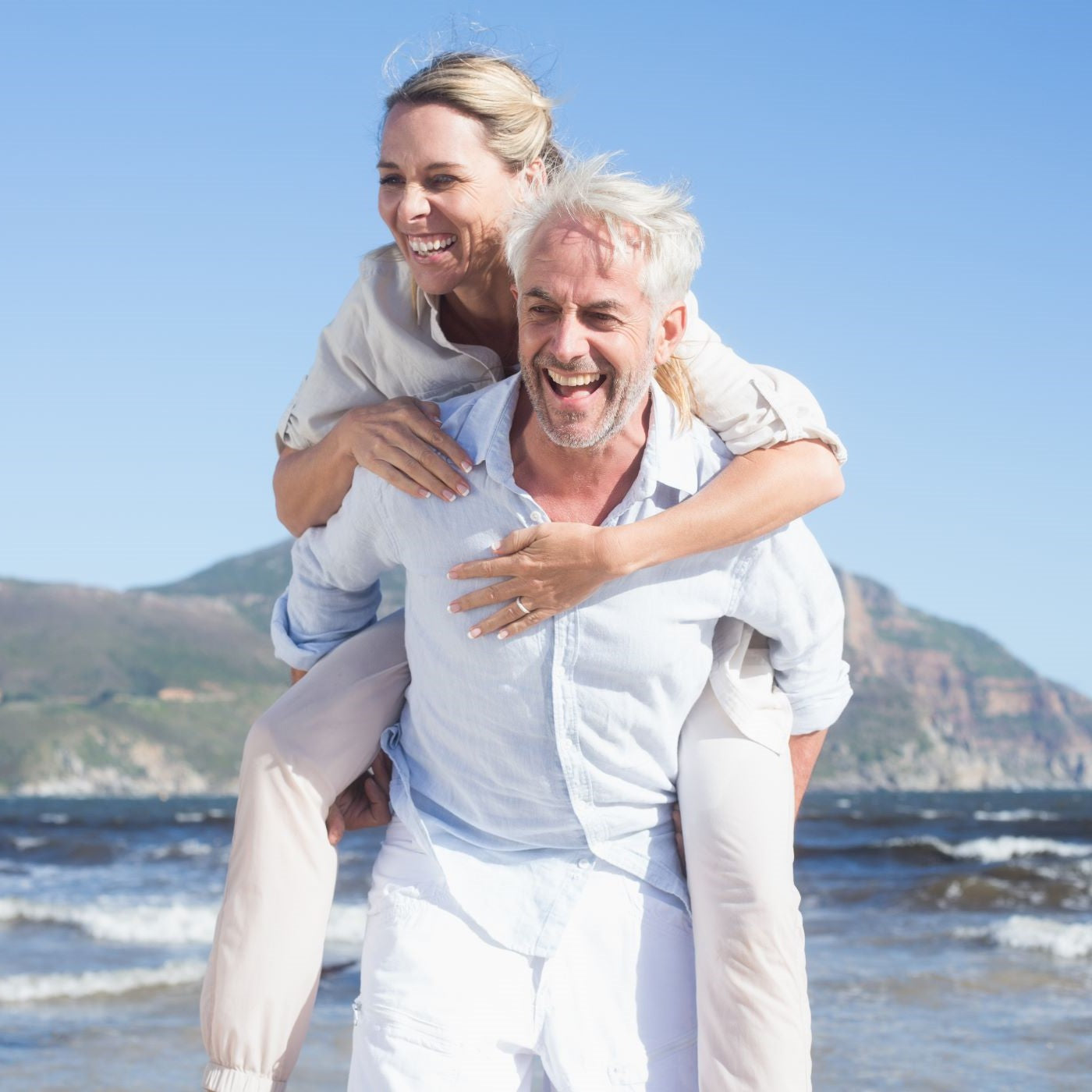Mann trägt Frau am Strand Huckepack